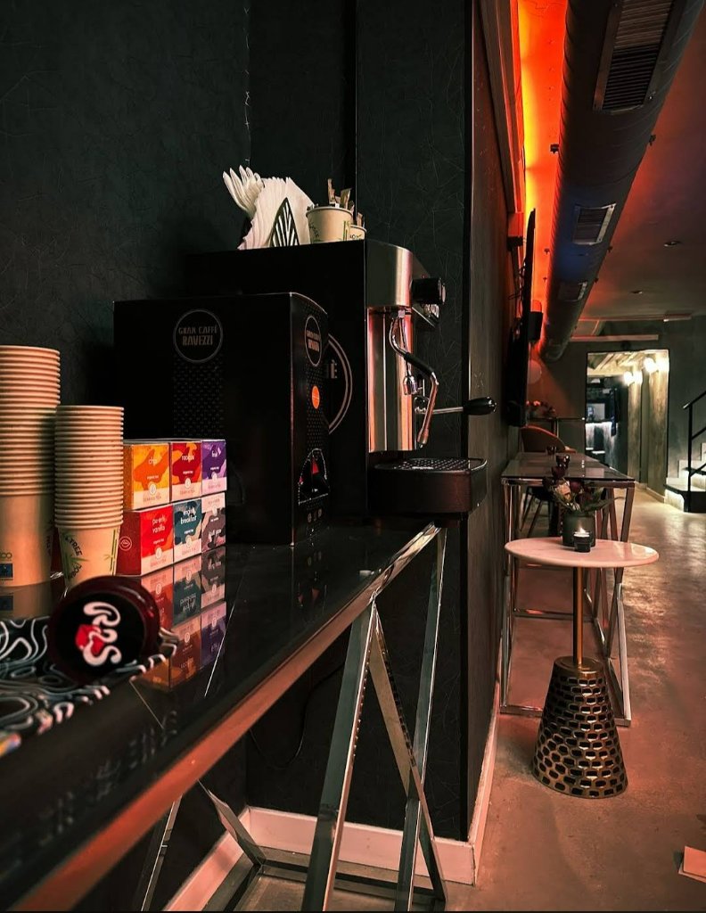 Zona de café del club Rolling Stoned en Barcelona con cafetera, vasos y mesas altas en el interior